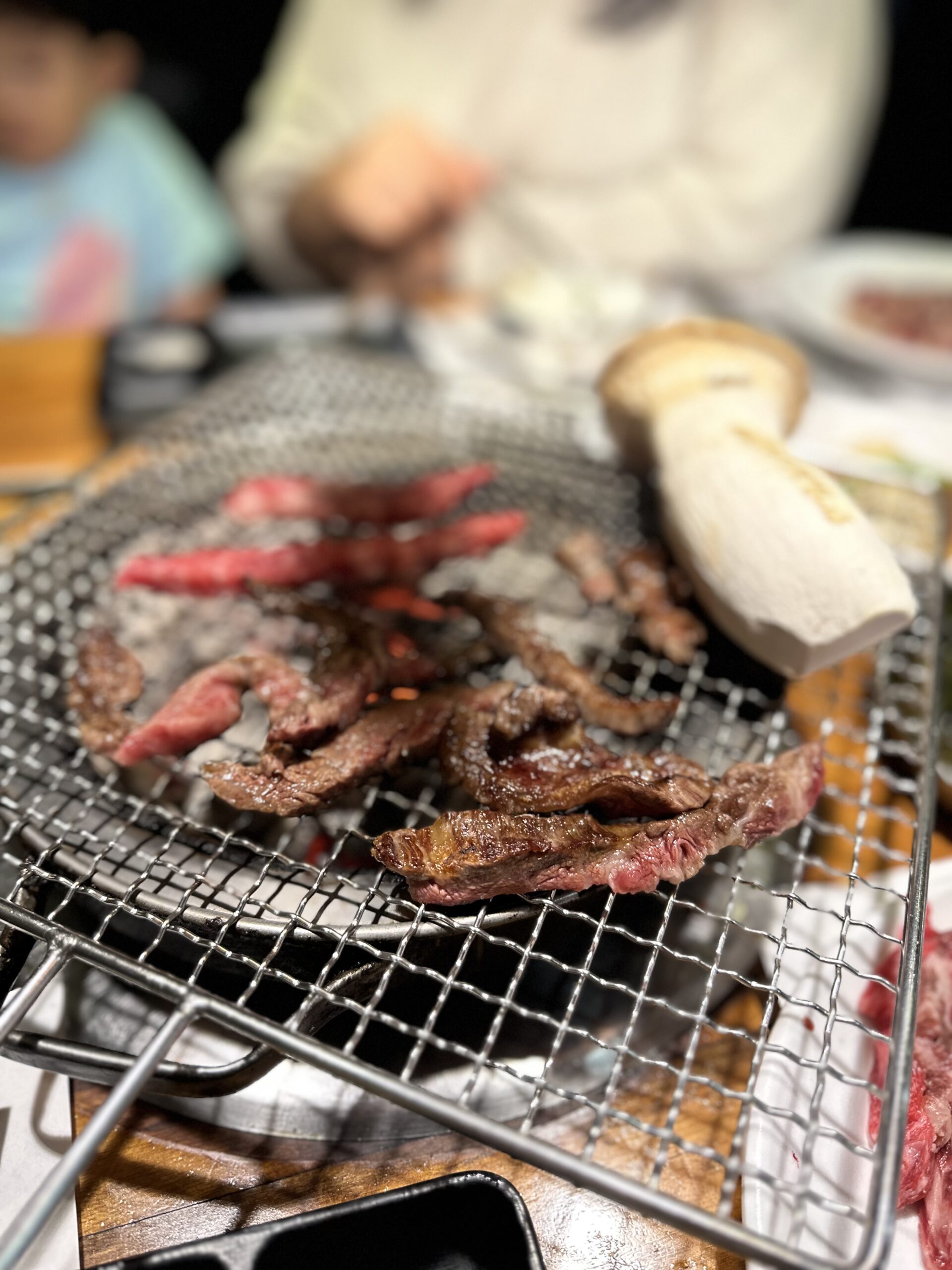A family with a child sharing a Korean BBQ meal, with beef and king oyster mushrooms on the grill
