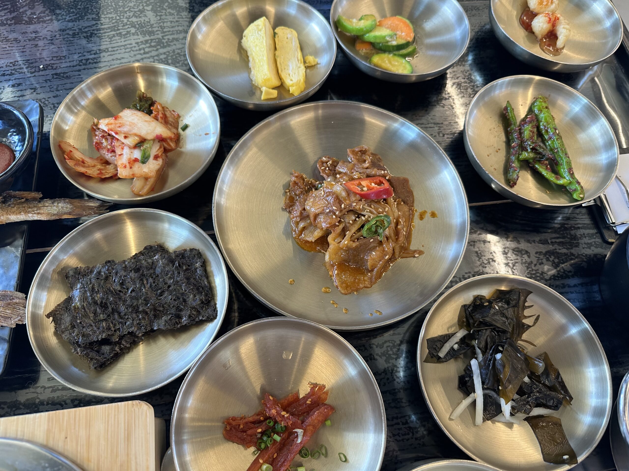 Assorted Korean banchan side dishes in stainless steel bowls — kimchi, seasoned vegetables, and egg at a local Korean restaurant