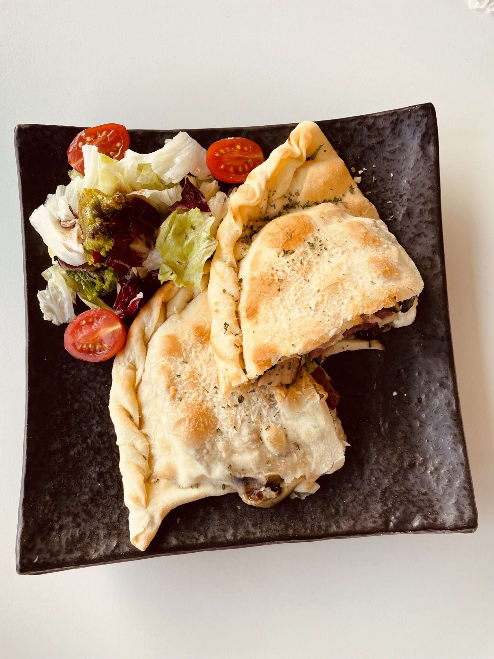 A baked stuffed flatbread topped with parmesan and herbs, served with a fresh side salad — Western-style cafe fare in Korea